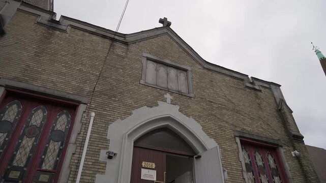 Brick Church Facade Under Overcast Sky, LowAngle View Showing Arched Doorway, Stained Glass Windows, Weathered Masonry And Distant Copper
