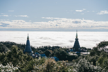 Two pagodas rise above a sea of clouds, framed by lush greenery and a blue sky, creating a serene and majestic landscape.