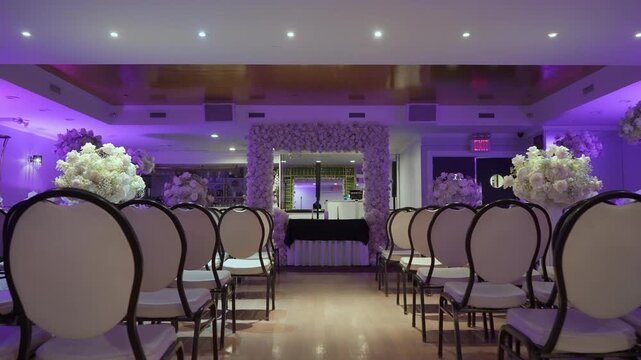 Empty Ceremony Aisle With Purple Lighting, Rows Of Elegant Chairs And Floral Pedestals, Vintage Mirror Backdrop And Soft Hardwood Floor,