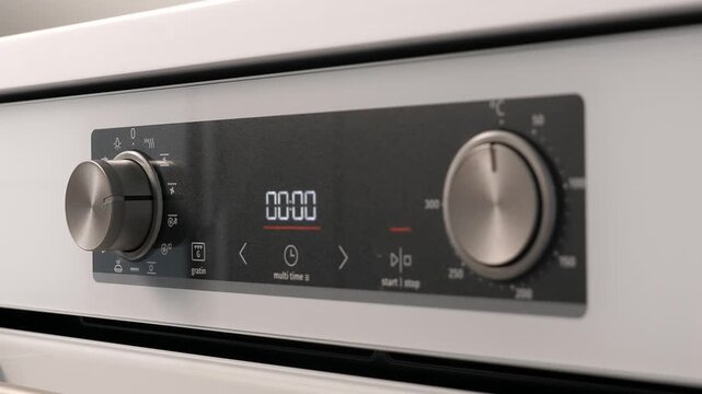 Woman adjusting modern white oven in kitchen. Female hand pushing and turning knobs on oven control panel. Closeup