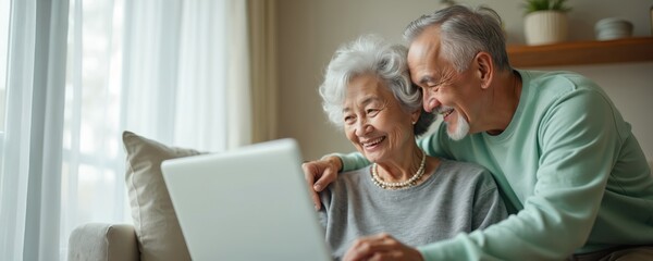 Elderly Asian couple sits on couch smiling while looking at laptop screen. Husband hugs wife from behind, happy family bonding. Mature seniors enjoy modern tech together indoors.