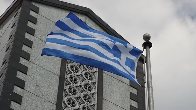 Greek Flag Waving Beside Ornate FaAde, Blue White Stripes Ripple In Gusty Wind Against Cloudy Sky, Flag Mounted On Polished Pole