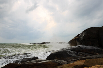 Obraz premium Under a cloudy sky, the waves crashed against the massive rocks, creating huge surges. (Scenic view of Hainan Stone Park, China) 