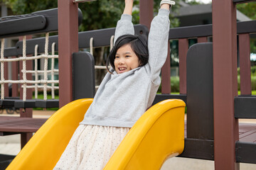 Excited Asian girl sliding quickly down a bright yellow playground slide, shouting with joy and adrenaline © Kwangmoozaa