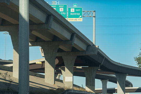 Elevated highway ramps in Texas with road signs showing East Bastrop Ramp 45 MPH and West City 71, blue sky and urban freeway view