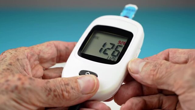 A person uses a white glucometer with blue accents to test blood sugar, set against a light blue background for healthcare monitoring.