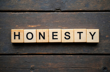 Fototapeta premium Wooden blocks spell out the word honesty on a dark textured table. This visual represents integrity, truth, and sincerity in a simple concept.