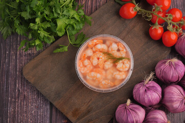 Shrimp in bowl with vegetables on wooden cutting board