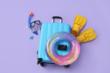 Suitcase with camera, inflatable ring, snorkeling flippers and mask on purple background © Pixel-Shot