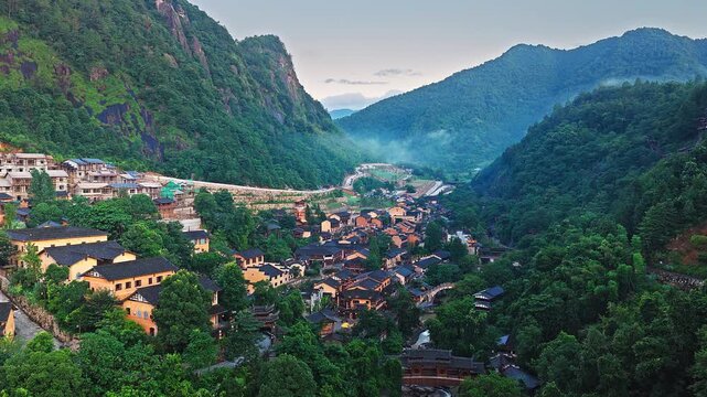 Aerial shot of traditional ancient village with classic architecture in a lush green mountain valley at dusk. The famous Wangxiang Valley Scenic Area is located in Jiangxi, China.