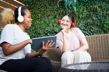 Young Women Sharing Digital Content on Terrace, Diverse Friends Collaborating with Tablet and Headphones Outdoors, Two Female Friends Enjoying Music and Media