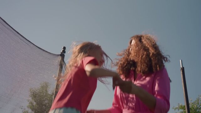 Playing Energetically Under Sunny Sky, Vibrant Scene Of Family Jumping On Trampoline In Sunlight, Carefree Mother And Daughter Engaging In Energetic Trampoline Play Outdoors In Bright Sunshine
