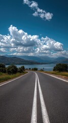 High quality photo of Scenic road curving towards a lake with distant mountains under a blue sky with clouds