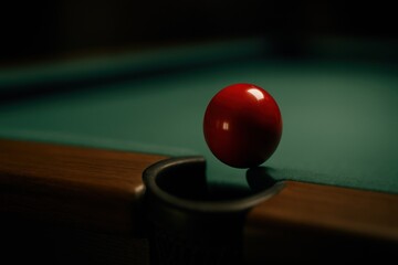 Red billiard ball resting on pool table pocket in dim light