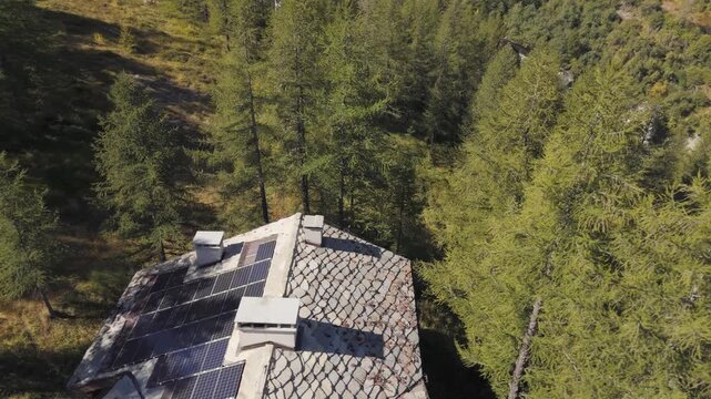 Aerial panning right of a hotel surrounded by tall pine trees in Italy, Aosta Valley, Valle d&rsquo;Aosta, showing the alpine landscape