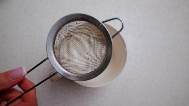 Woman's hand sets fine tea sieve over enamel cup for herbal infusion