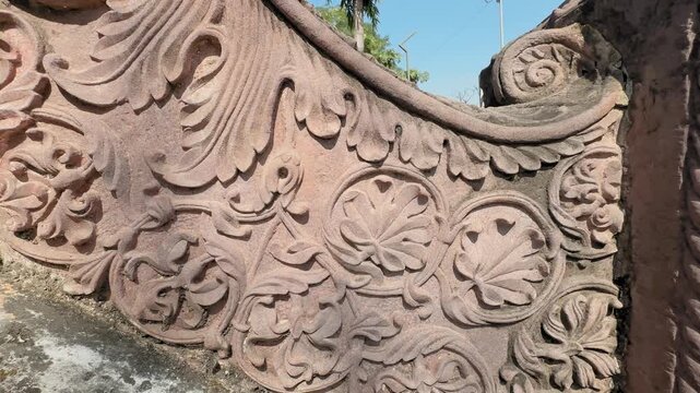 Camera tracks across an ornate stone carving filled with swirling floral motifs, rounded leaf patterns, and finely sculpted curves, highlighting the craftsmanship in warm sunlight.