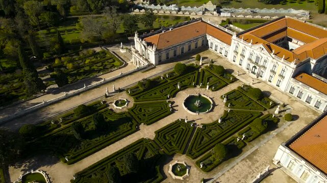 Aerial view of Queluz National Palace and its formal gardens in Portugal. Drone footage orbiting around the historic palace complex and landscaped gardens, showcasing elegant architecture and symmetry