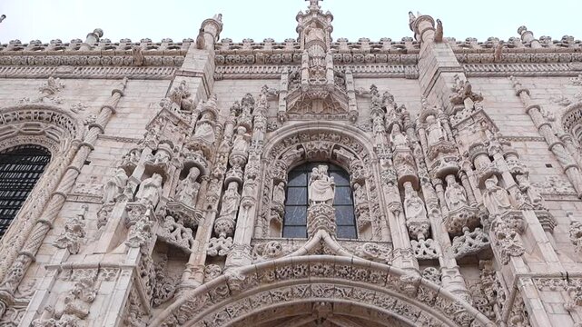 Exterior view of Jer&oacute;nimos Monastery in Lisbon Portugal. Ground-level camera movement from ornate roof details down to grand entrance doors, showcasing historic Manueline architecture, stone carvings.