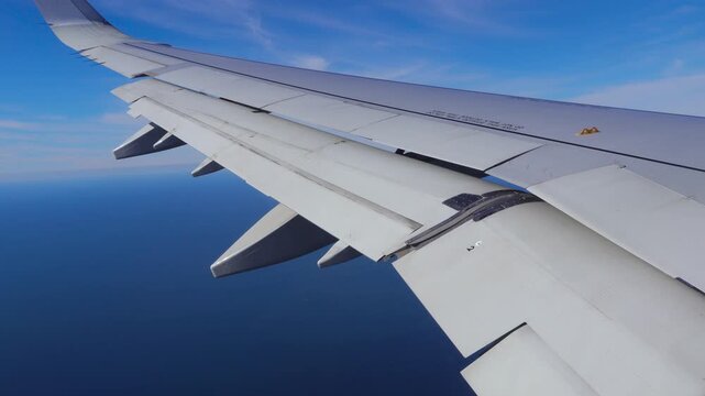 View from an airplane window showing the wing and moving flaps above the Atlantic Ocean near Lisbon Portugal during a sunny landing approach. Travel and aviation concept.