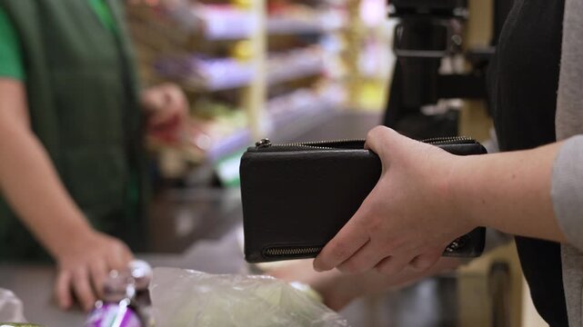 Woman paying cash at supermarket checkout taking banknote from wallet. Customer searching for coins in purse at grocery counter while finding small change for payment