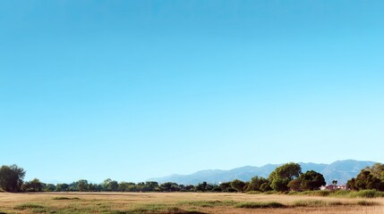 Obraz premium Serene Landscape with Clear Blue Sky Over Green Fields and Distant Mountain Range Under Bright Sunlight in a Tranquil Outdoor Setting