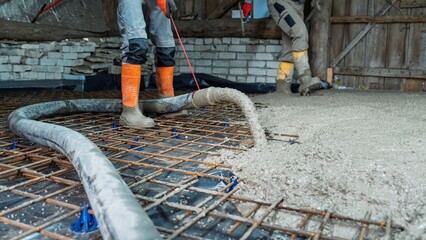 Construction worker using concrete pump to pour concrete slab for foundation. Reinforcement mesh is...