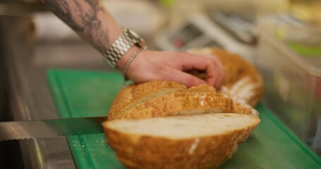 Cutting bread. Crispy crust pastry. Chef slicing wheat fresh loaf on kitchen board with knife. Baker hand preparing toasts ingredients.