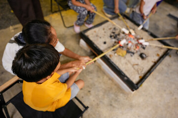A group of people holding chopsticks with marshmallows in their hands fries them on a fire. Picnic with friends. Hands without faces.