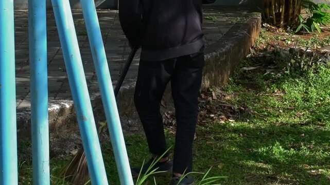 Middle-aged man sweeping fallen leaves with a traditional bidi broom in a park garden during the morning. This peaceful scene of routine maintenance is ideal for background footage.