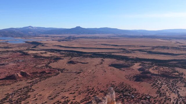 Drone footage advances steadily across open desert plains toward Cerro Pedernal, revealing winding land patterns, sparse vegetation, distant water, and layered horizons under clear blue skies.