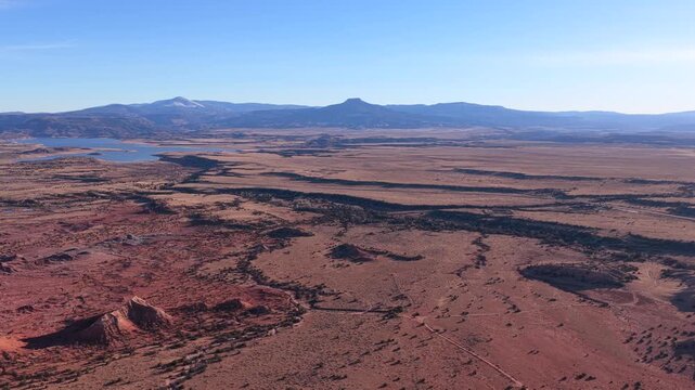 Drone footage moves steadily across expansive desert plains toward Cerro Pedernal, revealing winding land patterns, sparse vegetation, distant water, and layered terrain beneath clear blue skies.