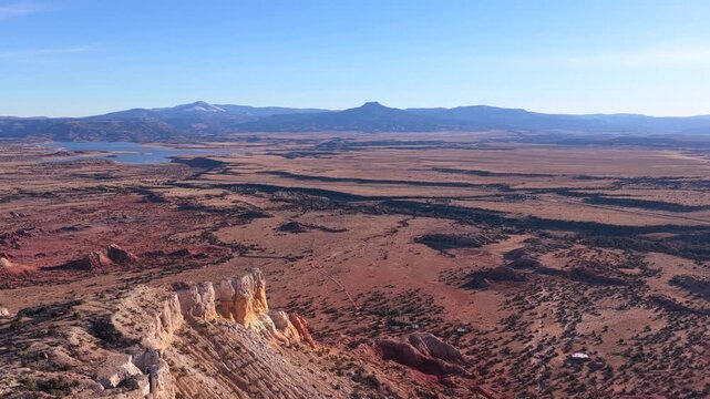 Drone footage floats above open desert plains and scattered red rock formations, revealing winding natural patterns, sparse vegetation, distant water, and Cerro Pedernal anchoring the horizon.