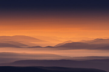 Obraz premium Vibrant sunset over misty mountain landscape with warm orange sky