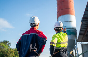 Two engineers standing on-site observing an industrial silo, discussing inspection results and operational planning in a factory environment.