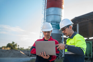 Two industrial engineers wearing safety helmets reviewing project information on a laptop at factory site, emphasizing digital workflow and on-site collaboration.