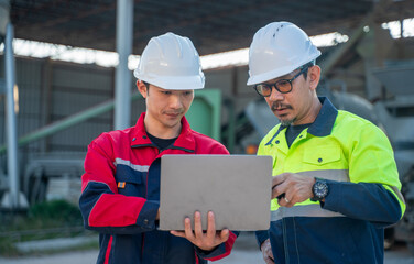 Engineers standing together in front of industrial silo while analyzing data on laptop, representing planning, inspection, and modern factory operations.
