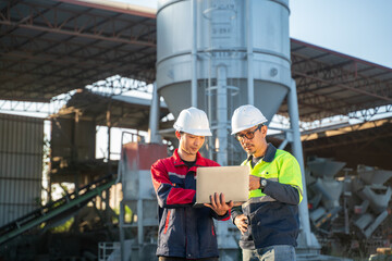 Two engineers focused on laptop screen while standing on industrial ground, symbolizing coordination, supervision, and field engineering management.