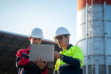 Engineers standing side by side at an industrial facility, carefully checking digital reports on a laptop during routine maintenance planning.