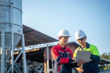 Two engineers reviewing production data on a laptop near large industrial equipment, representing modern industry and digital workflow integration.