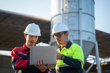 Engineers standing side by side at an industrial facility, carefully checking digital reports on a...