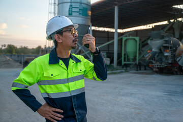 A safety officer communicating with crane operators or upper-level staff via radio to ensure site compliance near the storage tanks.