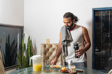Person standing at dining table with breakfast items and water bottle in home setting