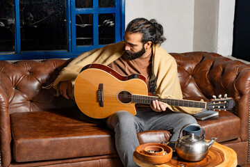 Person playing guitar with snacks and teapot on table in warm indoor setting