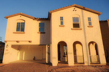 A newly completed stucco two-story home with arched entryways, finished exterior surfaces, and attached garage, illustrating modern residential construction and suburban housing development