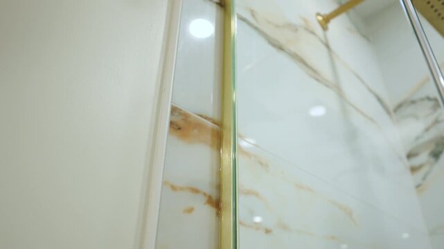Marble-style shower wall with elegant gold trim and hardware. Soft lighting highlights the luxurious materials and clean, contemporary interior design