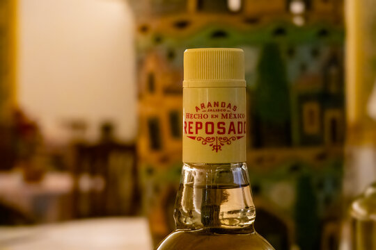 Huatulco, Oaxaca, Mexico. Dec 15, 2025. Close-up focus on the neck of a reposado tequila bottle featuring the Arandas, Jalisco label and a ribbed yellow cap, with a blurred background.