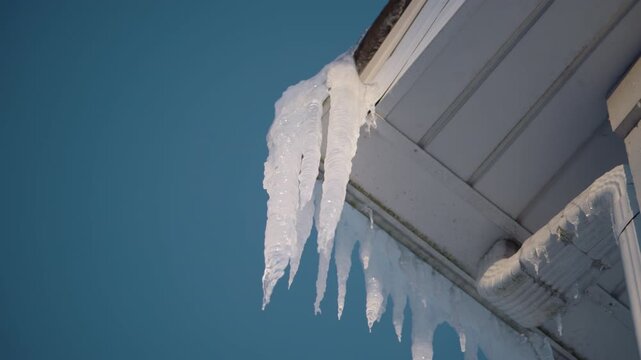Long, heavy sharp icicles forming along the edge of a roof and gutter on a cold winter day. View from below
