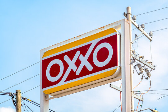 Huatulco, Oaxaca, Mexico. Dec 14, 2025. Close-up of the OXXO convenience store rectangular sign, with its red and white logo, mounted on a pole near power lines under a clear blue sky.