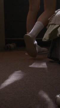 Vertical shot of unrecognizable woman in socks, wearing ankle monitor, stepping into her slippers upon waking up